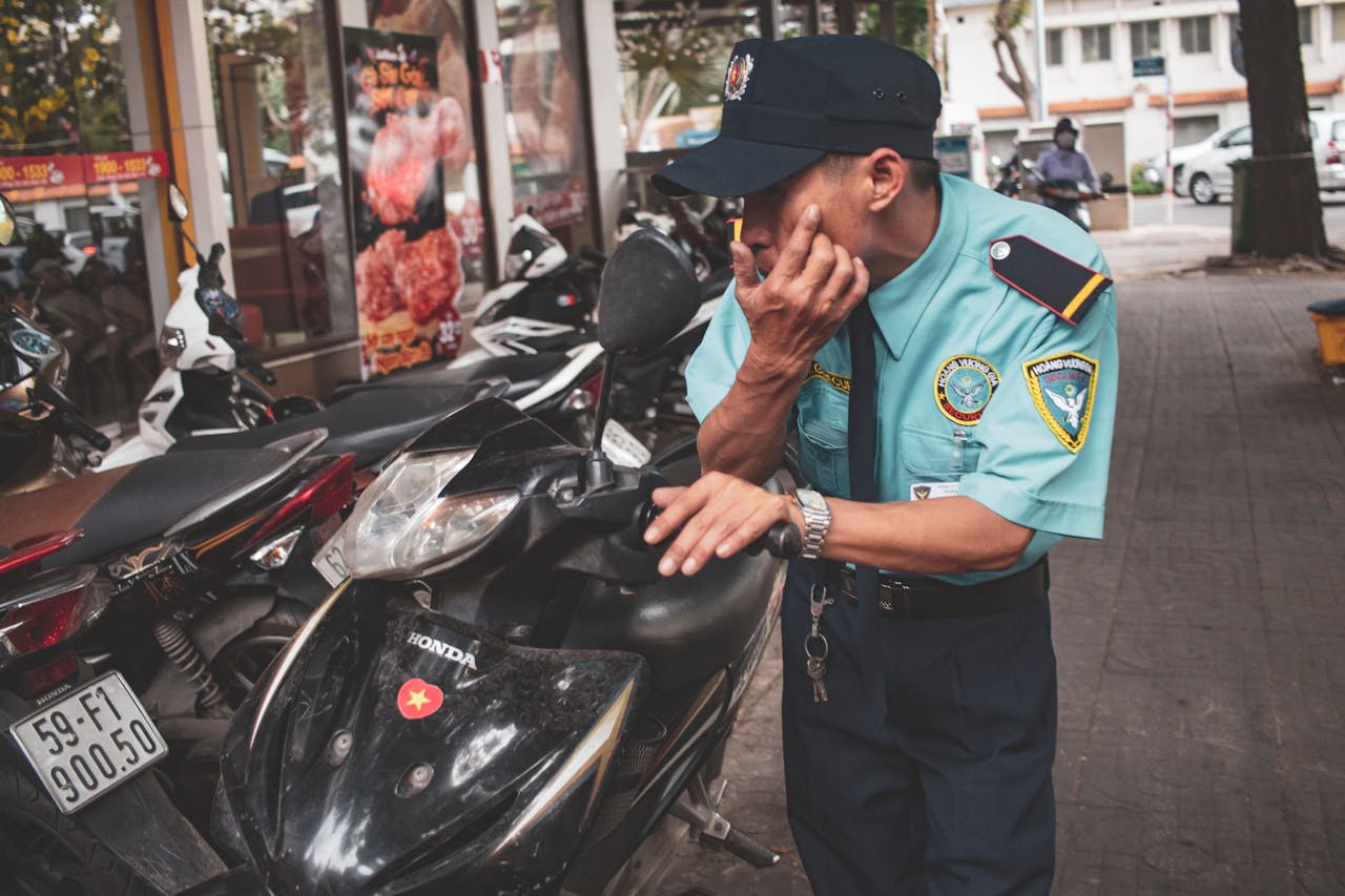 A policeman in uniform inspects a motor scooter on a busy city street corner.
