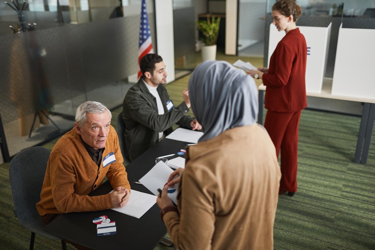 Adults engaging in the voting process at an indoor polling station, representing diverse backgrounds and social responsibility.